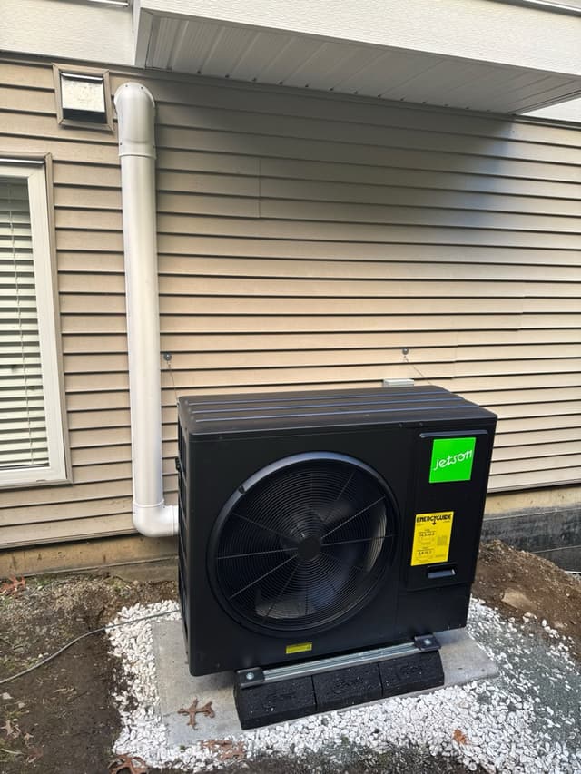 Black Jetson Air 3-ton heat pump on a gravel pad beside a beige-sided house in Abbotsford, BC, with a white line-set cover running up the wall.