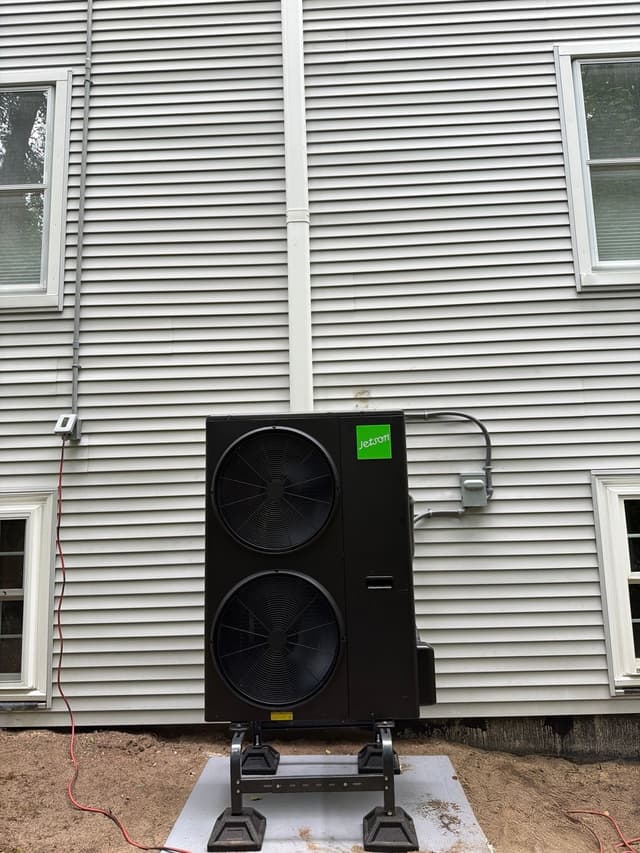 5-ton Jetson Air central ducted heat pump installed against gray vinyl siding of a home in Andover, MA, with white line-set conduit and electrical disconnect box visible.