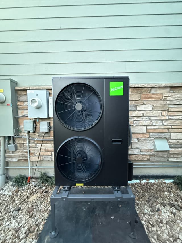 5-ton Jetson Air dual-fan outdoor heat pump unit installed alongside a home with stone veneer and lap siding in Aurora, with utility meter and disconnect boxes finished neatly to the left.