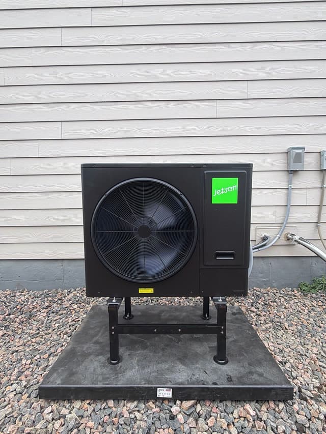 Jetson Air 3-ton heat pump condenser installed against gray lap siding of a home in Aurora, with refrigerant lines and disconnect box visible to the right.