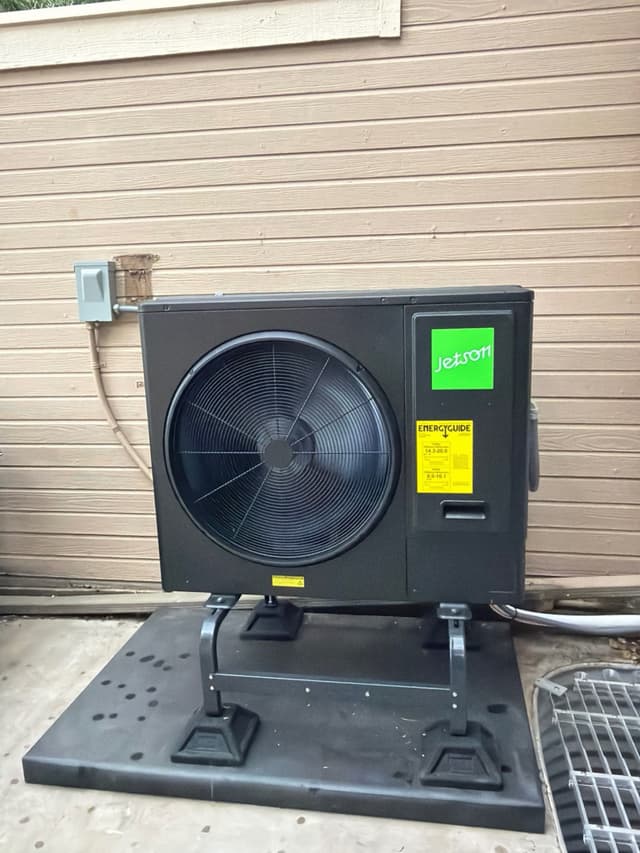 A black Jetson Air 3-ton heat pump mounted on an equipment stand against tan lap siding at an Aurora, CO home, with a disconnect box and conduit visible.