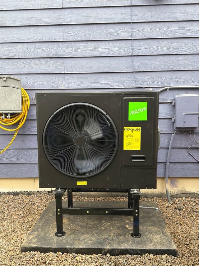 3-ton Jetson Air central ducted heat pump mounted on a black metal stand against blue lap siding at an Aurora home, with a gray electrical disconnect box and conduit visible to the right.