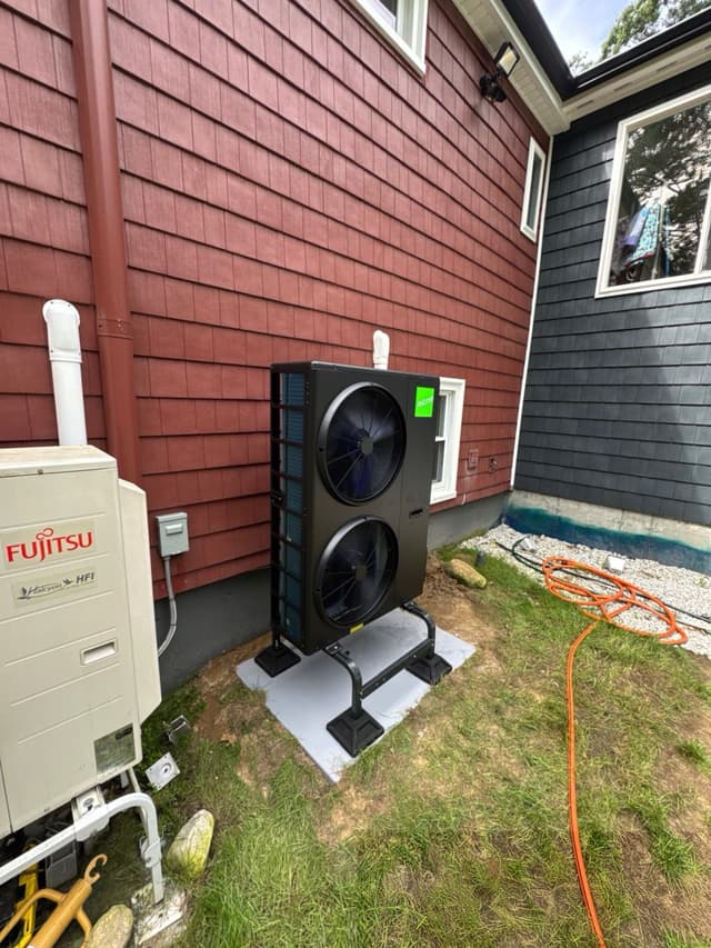 A 4-ton Jetson Air central ducted heat pump installed on the side of a house in Bellingham, MA, with a neighboring Fujitsu Halcyon outdoor unit visible to the left.