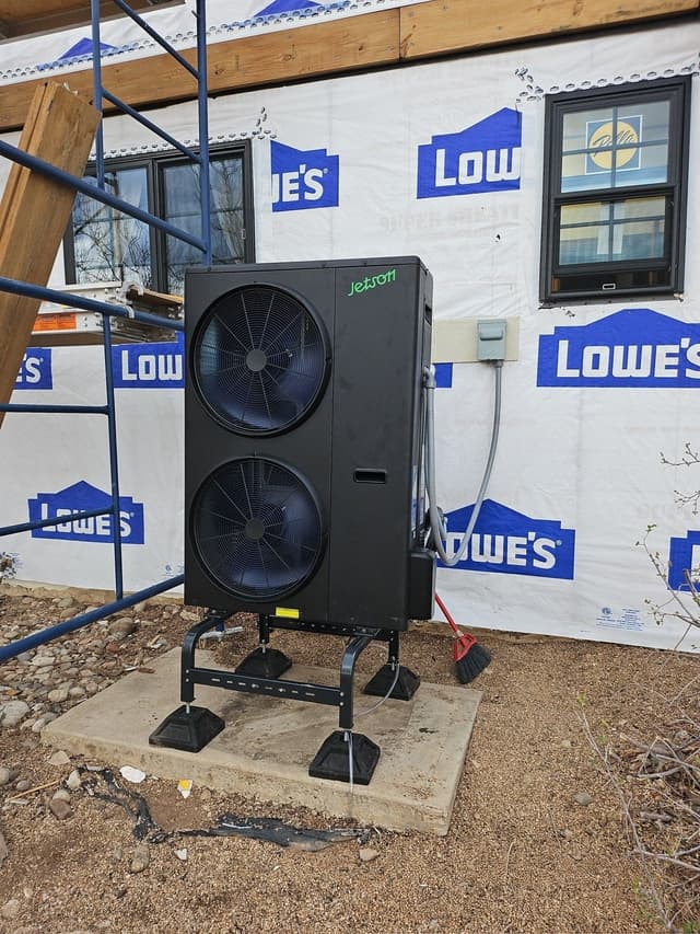5-ton Jetson heat pump condenser on a concrete pad outside a house under construction in Berthoud, CO, with house wrap and scaffolding visible in the background.