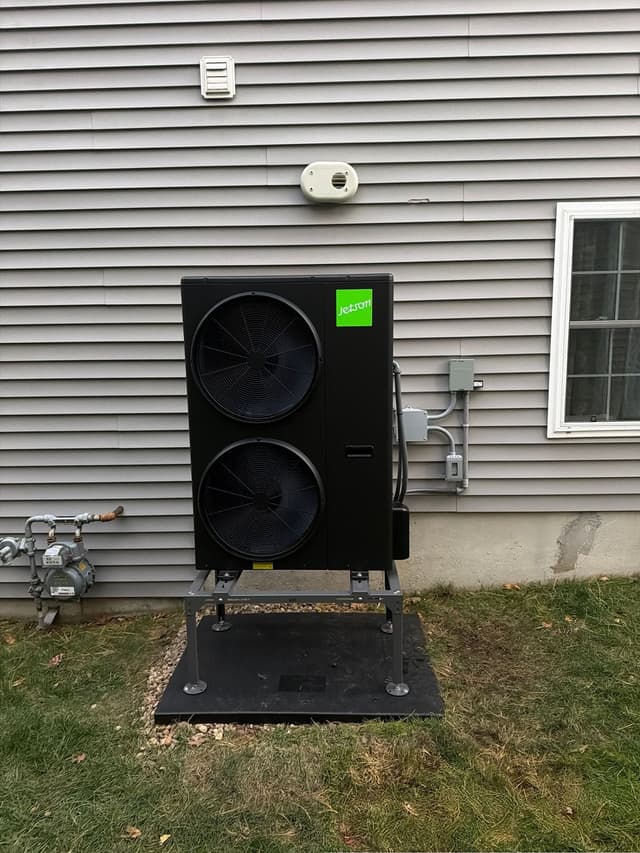 4-ton Jetson Air dual-fan heat pump condenser mounted on a metal equipment stand along gray vinyl siding in Billerica, MA, with conduit and electrical disconnect neatly run to the right.