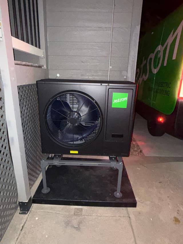 Jetson Air 3-ton central ducted heat pump installed against gray siding in a side yard at night, with a Jetson service van partially visible in the background.