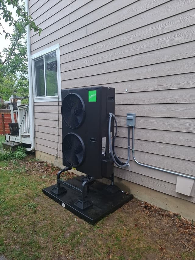A black Jetson Air 4-ton heat pump on an anti-vibration pad and riser stand mounted against gray vinyl siding at a residential home in Broomfield, CO, with a disconnect box and metal conduit to the right.