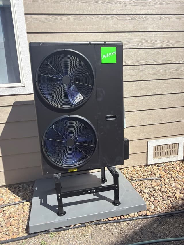 4-ton Jetson Air dual-fan outdoor heat pump condenser mounted on a black metal stand over a concrete pad, against tan lap siding of a Castle Pines, CO home.