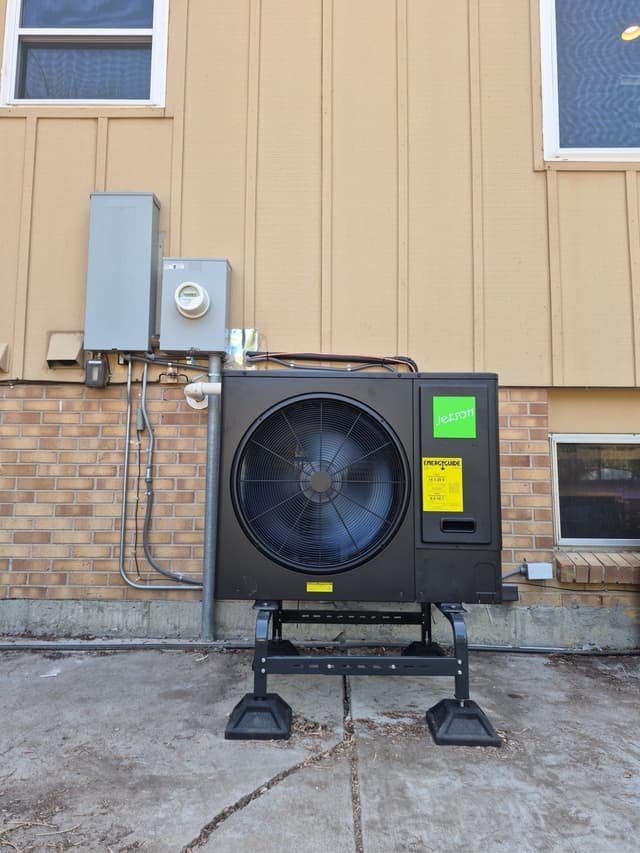 Jetson Air 3-ton central ducted heat pump mounted on a stand against the brick and tan siding exterior of a home in Centennial, Colorado, with refrigerant lines running to a disconnect box and utility meter.