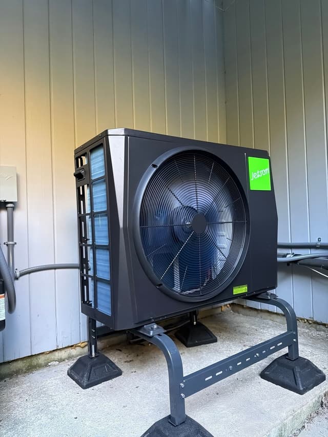 Jetson Air 2-ton heat pump outdoor unit installed against a light gray vertical-panel wall in Chappaqua, NY, with lineset and conduit running to an electrical disconnect box.