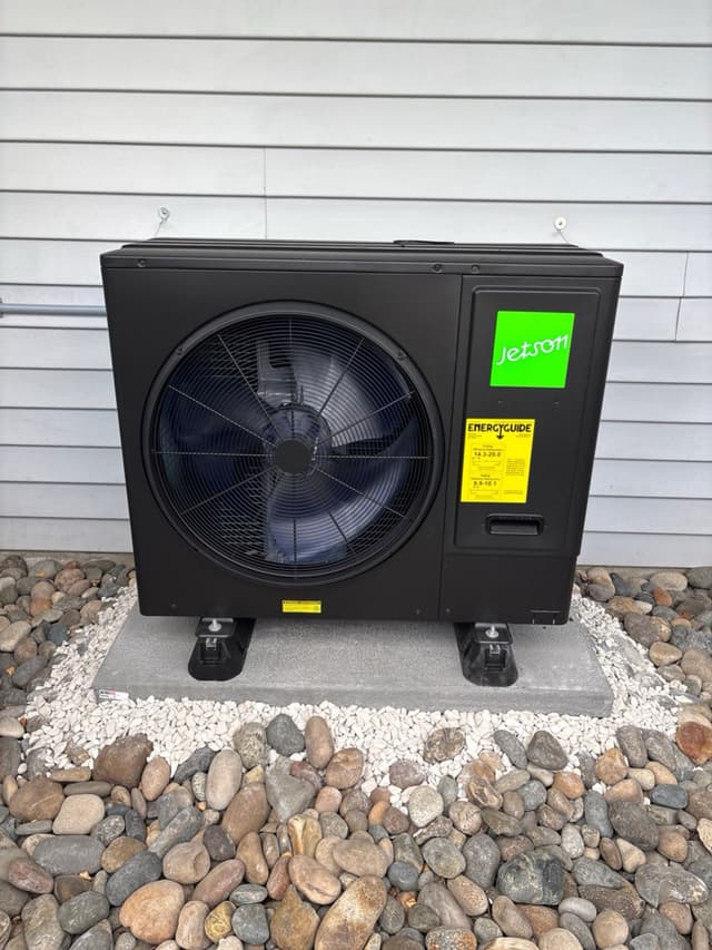Jetson Air 3-ton heat pump on a concrete pad with white gravel and river rocks, grey horizontal siding in background, Coquitlam BC.