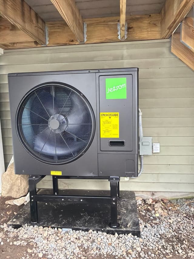 Jetson Air 3-ton heat pump condenser on a metal stand over a concrete pad and gravel bed, mounted beneath a covered deck at a home in Everett, MA.