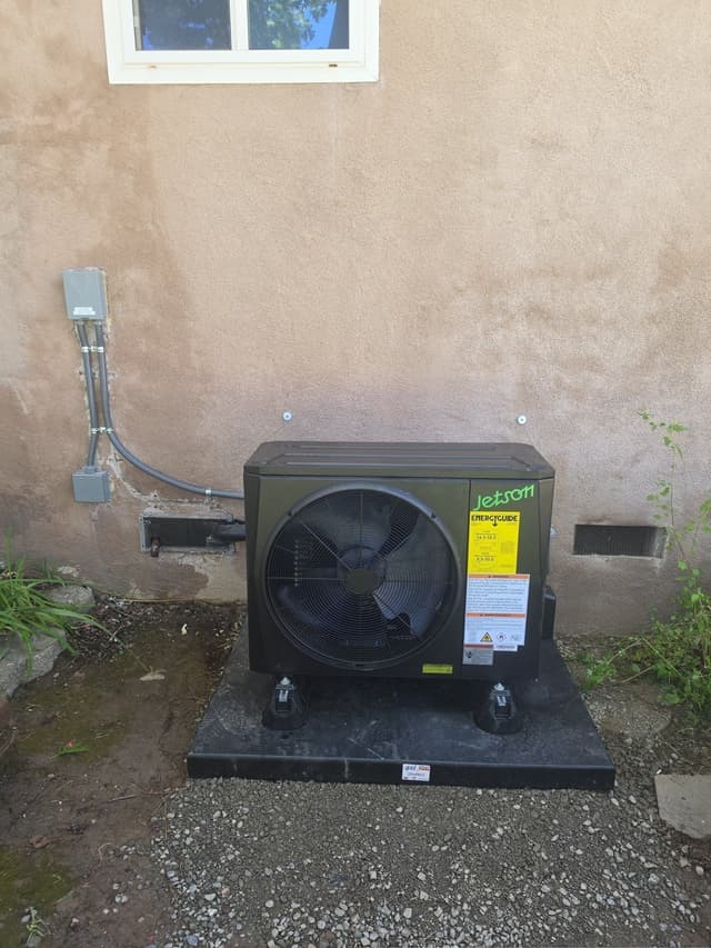 Black Jetson Air 2-ton central ducted heat pump unit mounted on a pad against a tan stucco wall at a Fair Oaks home, with conduit running to an electrical disconnect box.