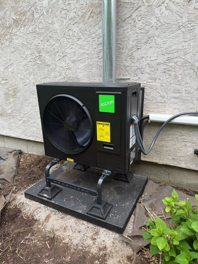 Black Jetson Air 3-ton heat pump mounted on a metal stand against a stucco exterior wall at a home in Framingham, MA.