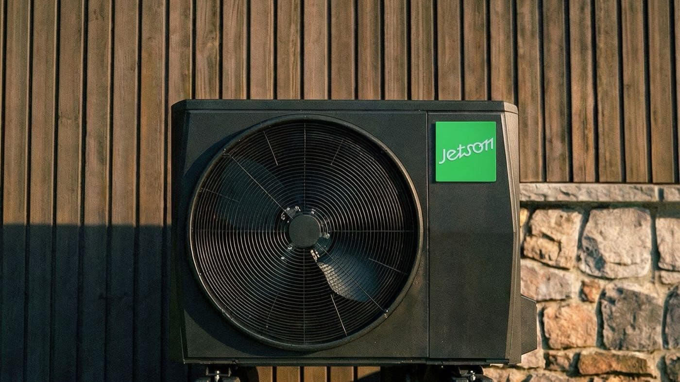 Jetson heat pump condenser against a wood-slat wall on a sunny lawn