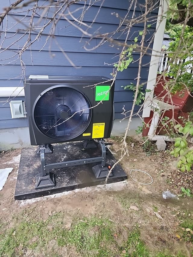Black Jetson Air 2-ton central ducted heat pump installed against blue vinyl siding of a home in Hartsdale, NY.