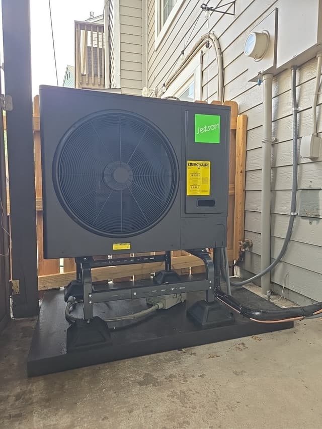 Black Jetson Air 3-ton heat pump condenser on an elevated metal stand against gray house siding in Lakewood, CO, with refrigerant lines and conduit running neatly to the wall.