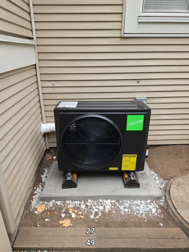 Jetson Air 2-ton central ducted heat pump installed against the beige vinyl siding of a Langley home, with white gravel on the ground around it.