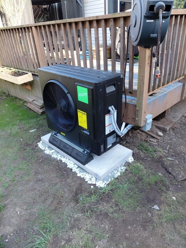 Black Jetson Air 3-ton heat pump condenser on a concrete pad with white gravel, installed beside a wooden deck in a Langley, BC backyard.