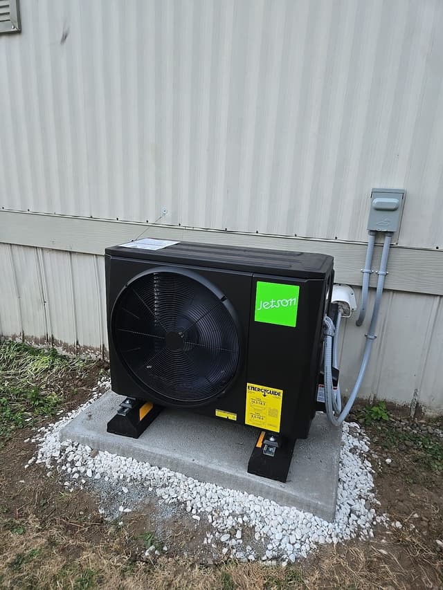Jetson Air 2-ton outdoor heat pump unit installed against corrugated metal siding in Walnut Grove, Langley, with conduit running up to a gray electrical disconnect box.