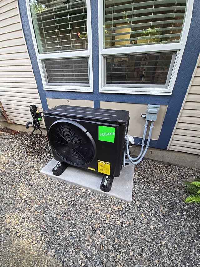 Jetson Air 2-ton heat pump condenser mounted on a concrete pad alongside a lap-siding house in Murrayville, Langley, with refrigerant lines running up to a wall-mounted disconnect box.