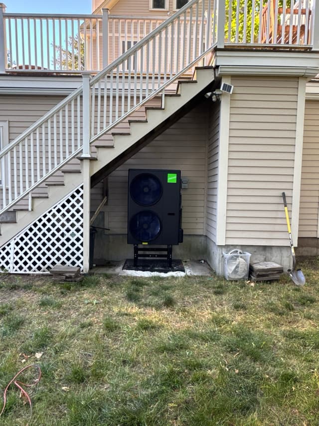 Jetson Air 4-ton heat pump installed on a metal stand under an exterior staircase on the side of a house in Lexington, MA.