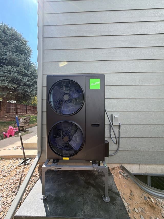 4-ton Jetson Air dual-fan heat pump condenser installed alongside a gray-sided house in Littleton, with rock landscaping and a wooden fence visible in the background.