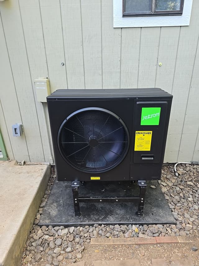 3-ton Jetson Air central ducted heat pump mounted on an elevated stand beside a light green vertical-board house in Longmont, Colorado.