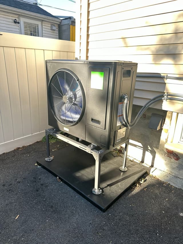 Jetson Air 3-ton central ducted heat pump outdoor unit installed along the side of a house with tan siding and a white vinyl fence in Malden, MA.