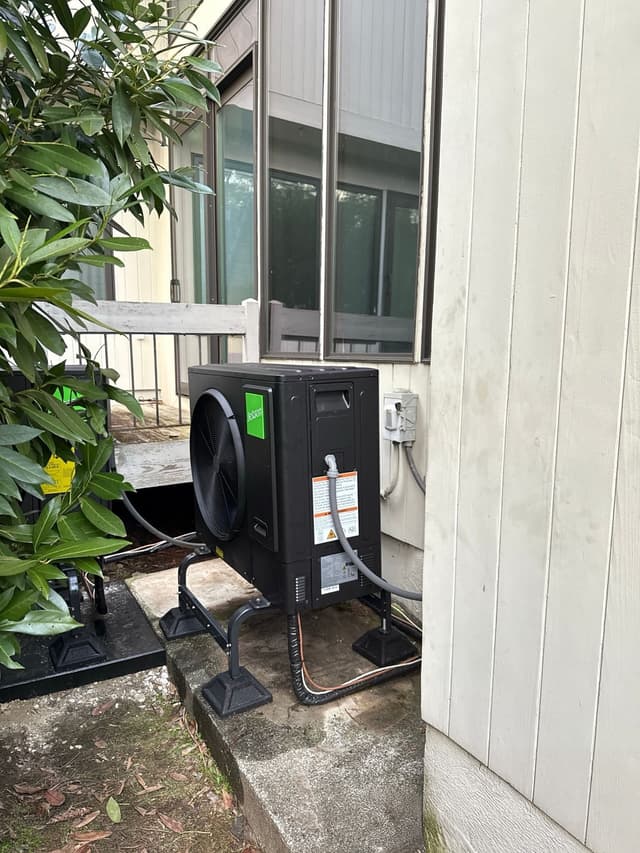 Jetson Air 3-ton central ducted heat pump condenser installed beside a white-sided house in Mamaroneck, NY, with line set and conduit running into the exterior wall and a large shrub to the left.