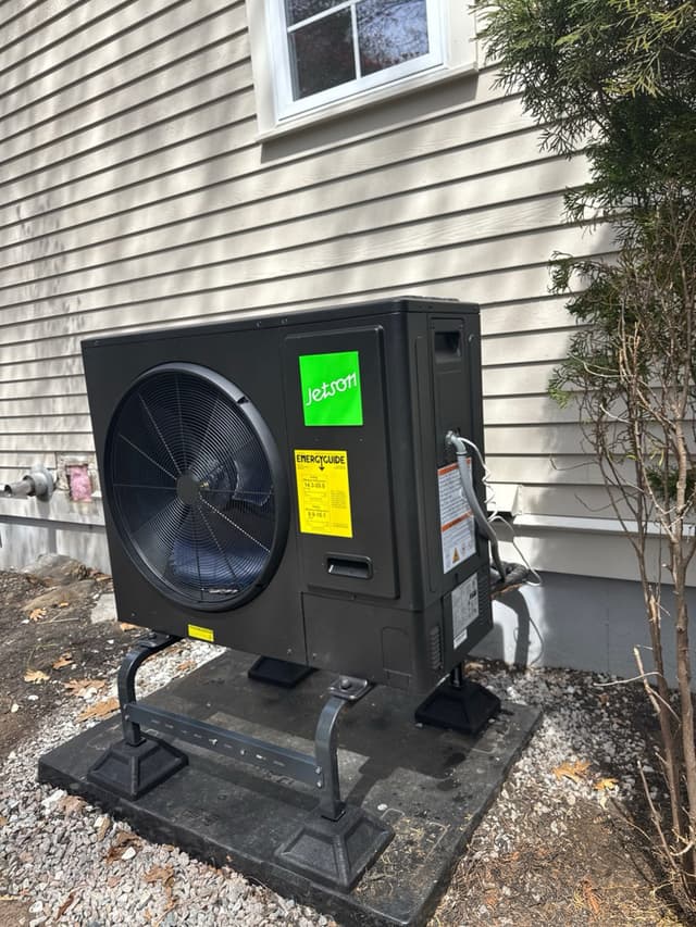 3-ton Jetson Air outdoor heat pump mounted on a raised anti-vibration stand on a gravel surface along the side of a beige house in Marlborough, MA.