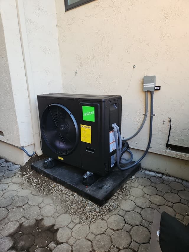 Black Jetson Air 3-ton heat pump installed against a stucco exterior wall on a paver surface in Mountain View, CA, with refrigerant lines and conduit running to a wall-mounted disconnect box.