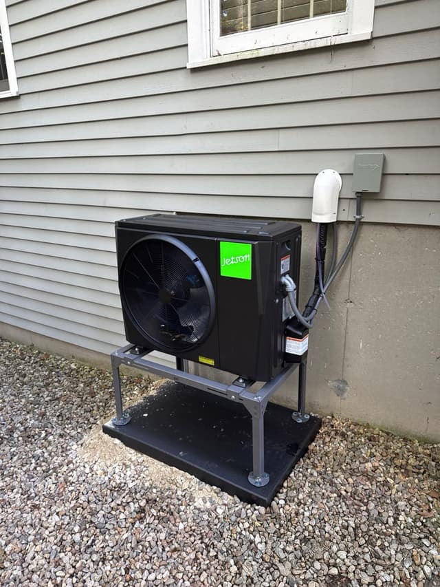Jetson Air 2-ton central ducted heat pump condenser mounted along the side of a gray-sided house in North Andover, with conduit and disconnect box visible on the wall.
