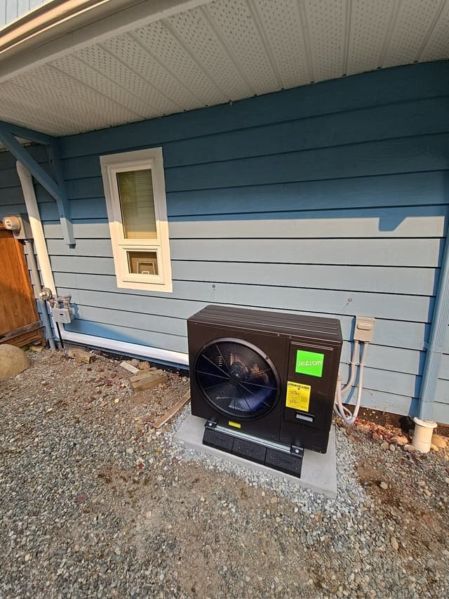 Black Jetson Air 3-ton heat pump installed beside a blue lap-sided house in Lynn Valley, North Vancouver, with electrical disconnect and meter panel visible.