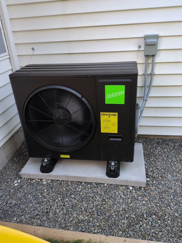 Jetson Air 3-ton central ducted heat pump installed on a gravel bed beside a white-sided house in Seymour, North Vancouver, with electrical conduit and disconnect box mounted on the wall.