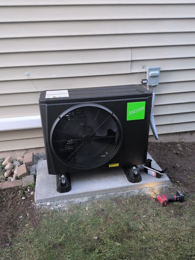 Jetson Air 2-ton heat pump installed on a concrete pad against beige vinyl siding in Seymour, North Vancouver, with electrical disconnect box and conduit on the wall beside it.