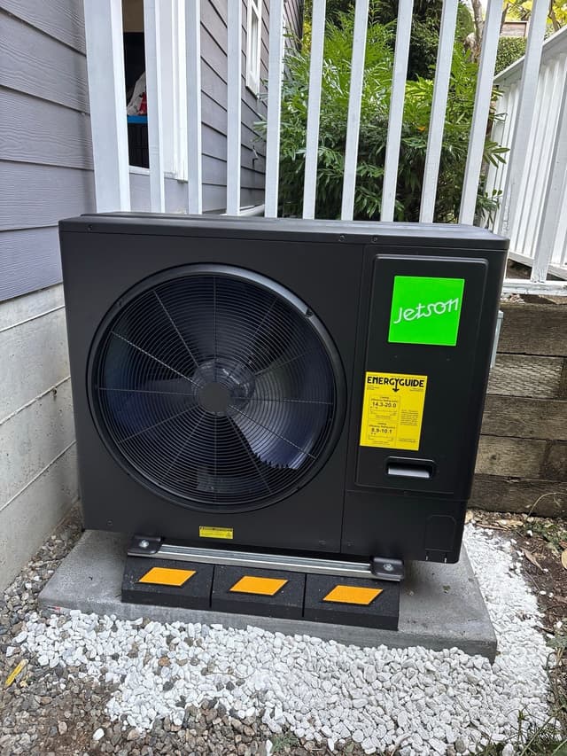 Jetson Air 3-ton central ducted heat pump installed in a side yard between grey lap siding and a white wooden fence in Delbrook-Upper Lonsdale, North Vancouver.