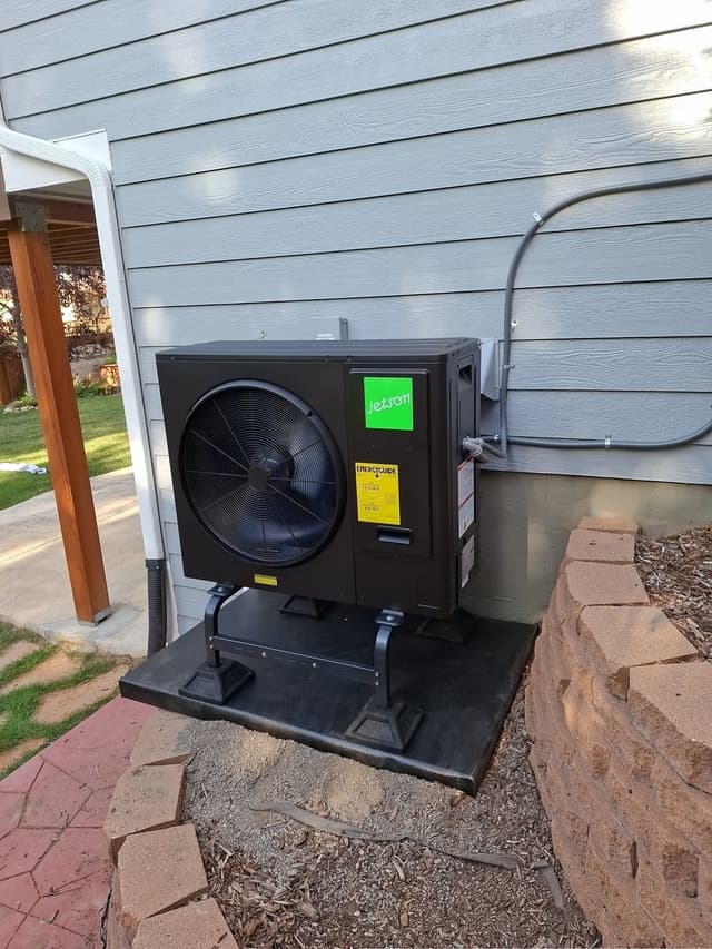 Jetson Air 3-ton central ducted heat pump mounted against gray lap siding on a residential home in Parker, CO, with electrical conduit running up to a disconnect box and mulched garden beds along the base.