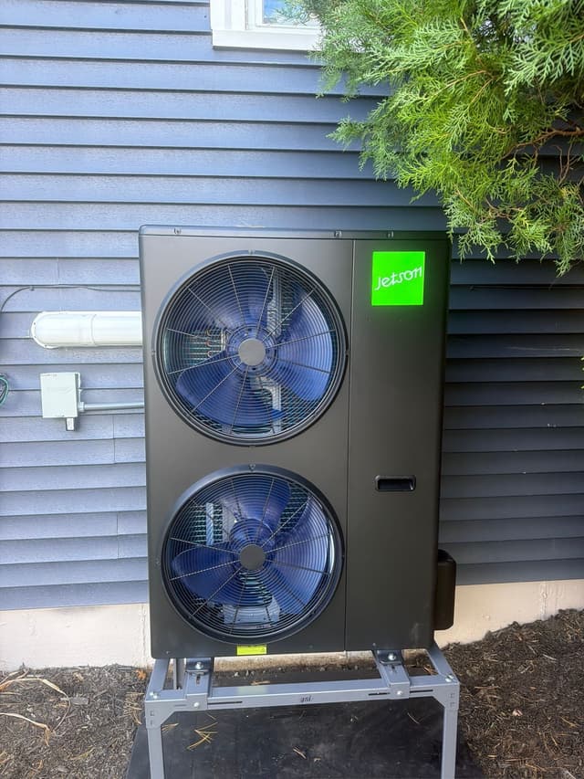 5-ton Jetson Air dual-fan outdoor heat pump unit installed against the gray siding of a home in Peabody, MA, with a white line set cover and disconnect box visible to the left.