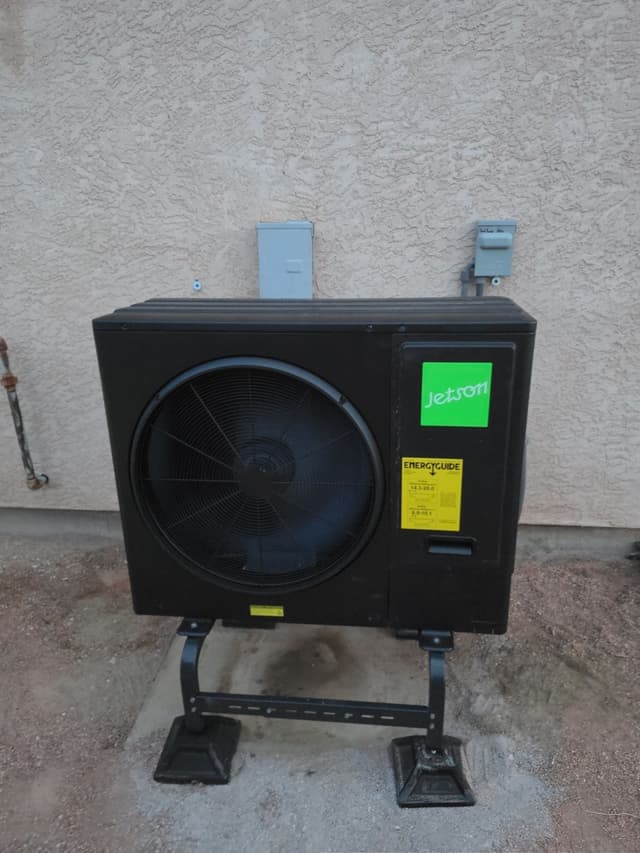 A 3-ton Jetson Air central ducted heat pump installed against a beige stucco exterior wall in Pueblo West, Colorado, with two gray electrical disconnect boxes mounted on the wall behind it.