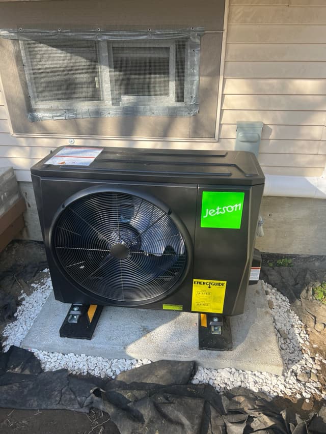 Jetson Air 2-ton outdoor heat pump unit on a concrete pad with anti-vibration feet, surrounded by white gravel, against a beige-sided house in Richmond, BC.