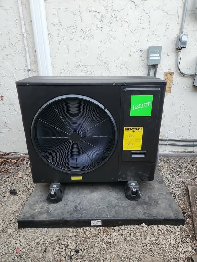 Black Jetson Air 3-ton heat pump outdoor unit installed against a stucco exterior wall in San Jose, with disconnect box and conduit visible above.