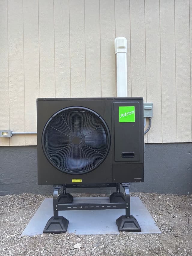 Jetson Air 3-ton central ducted heat pump outdoor unit mounted on a gravel surface against a board-siding wall in Stoughton, MA.