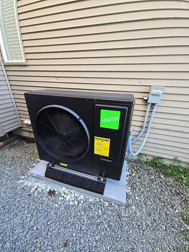 Jetson Air 3-ton heat pump mounted on a concrete pad beside tan vinyl siding in Clayton Heights, Surrey, with white conduit running neatly to a disconnect box above.