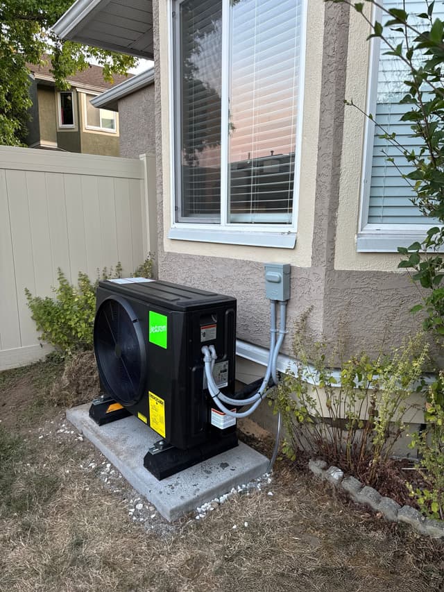 Black Jetson Air 2-ton heat pump condenser installed along the side of a stucco home in Fleetwood, Surrey, with grey conduit lines running to a wall-mounted disconnect box.