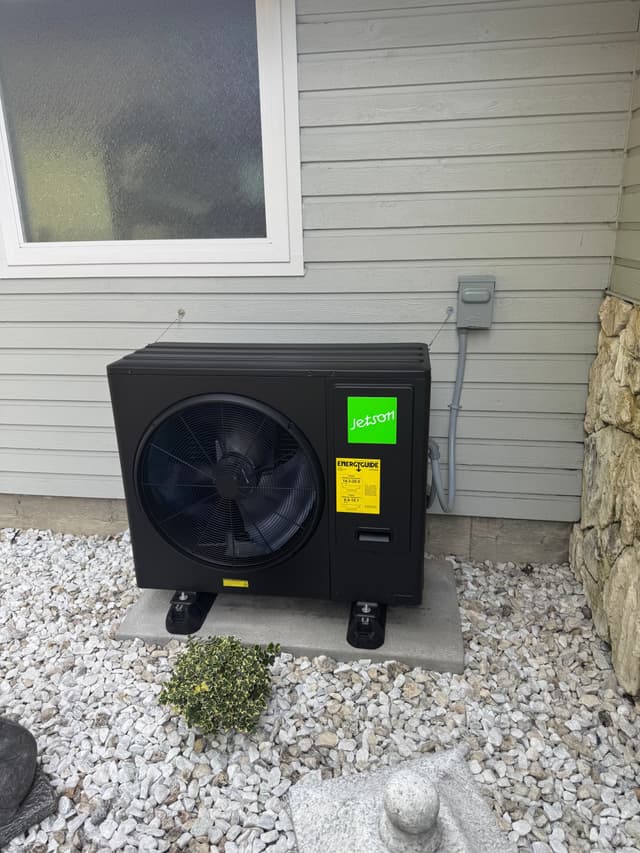 Jetson Air 3-ton heat pump installed against a light gray lap-siding house with white gravel and a stone wall to the right, Johnston Heights, Surrey.