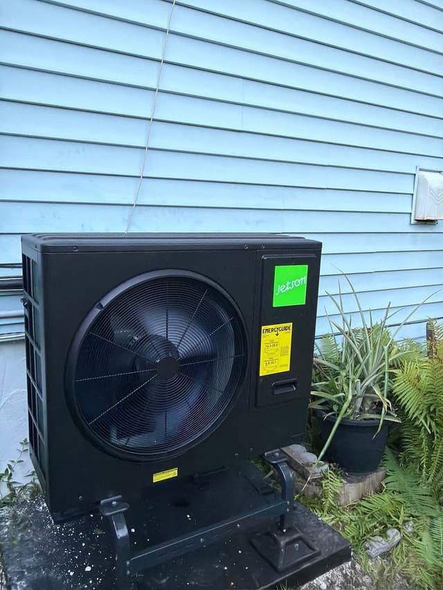 Black Jetson Air 3-ton central ducted heat pump condenser installed on a concrete pad against light-blue vinyl siding of a home in White Plains, NY.