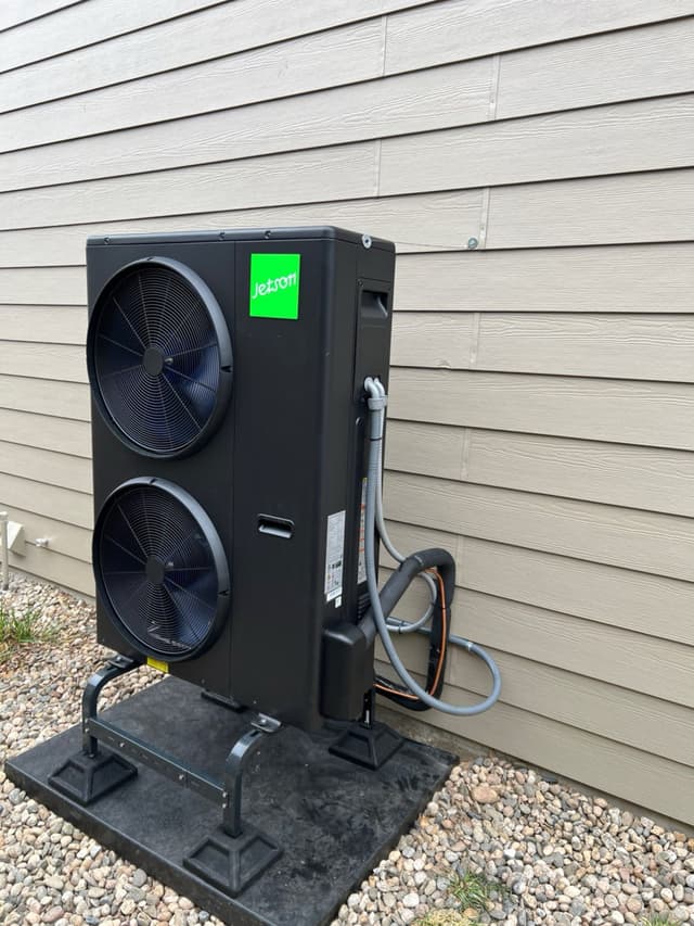 A 4-ton Jetson Air central ducted heat pump installed on a gravel pad against gray lap siding of a home in Windsor, CO, with refrigerant lines and conduit running neatly into the wall.