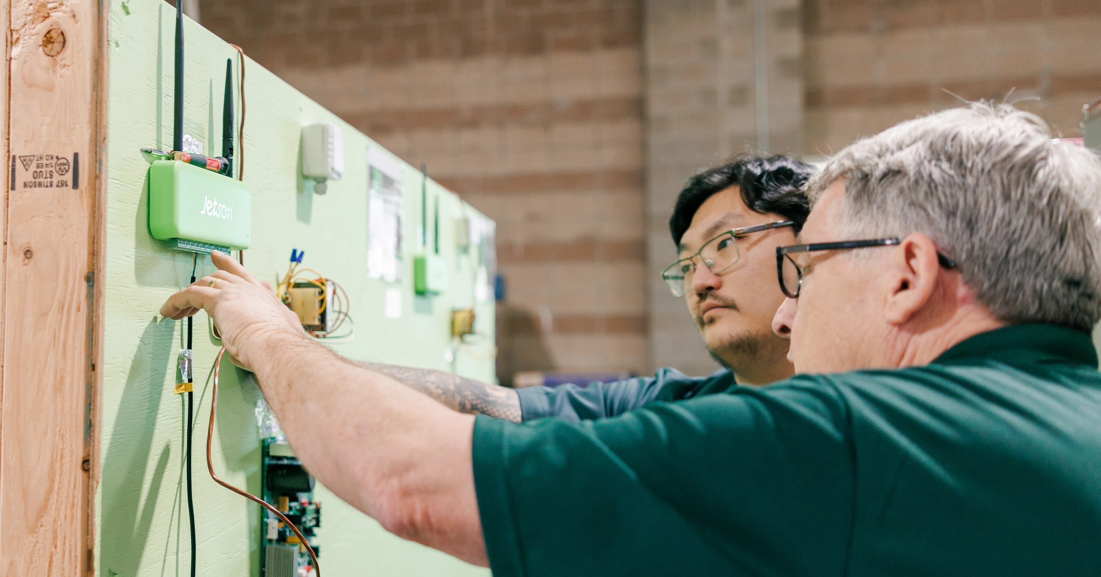 A JetStart instructor guiding a trainee as they wire a Jetson hub on a practice wall in the training facility
