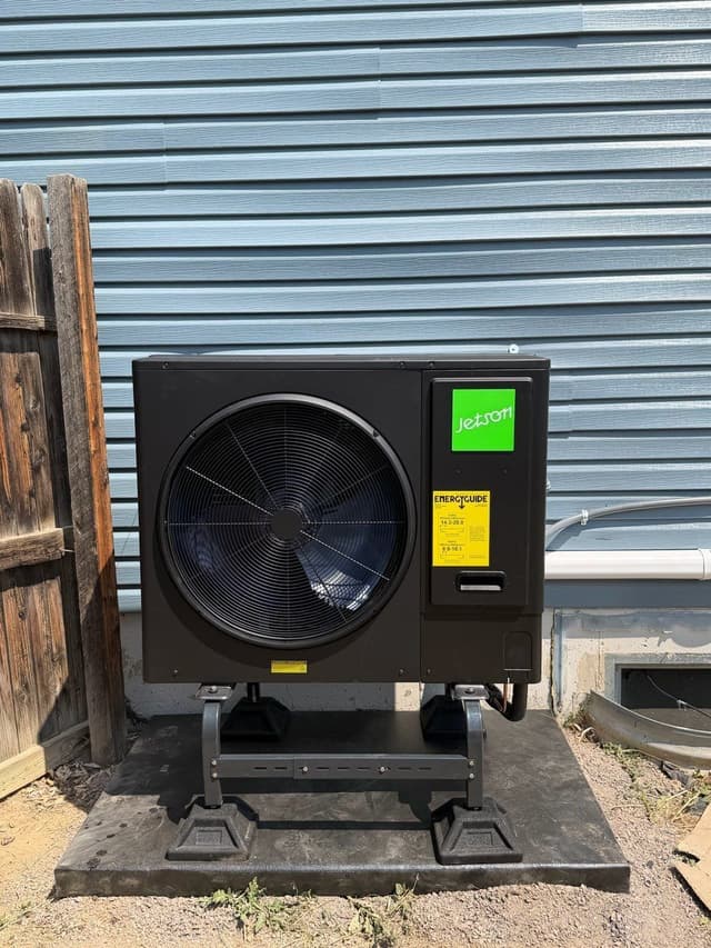 Jetson Air 3-ton central ducted heat pump on a riser pad beside a wooden fence and blue lap siding at an Aurora, CO home.